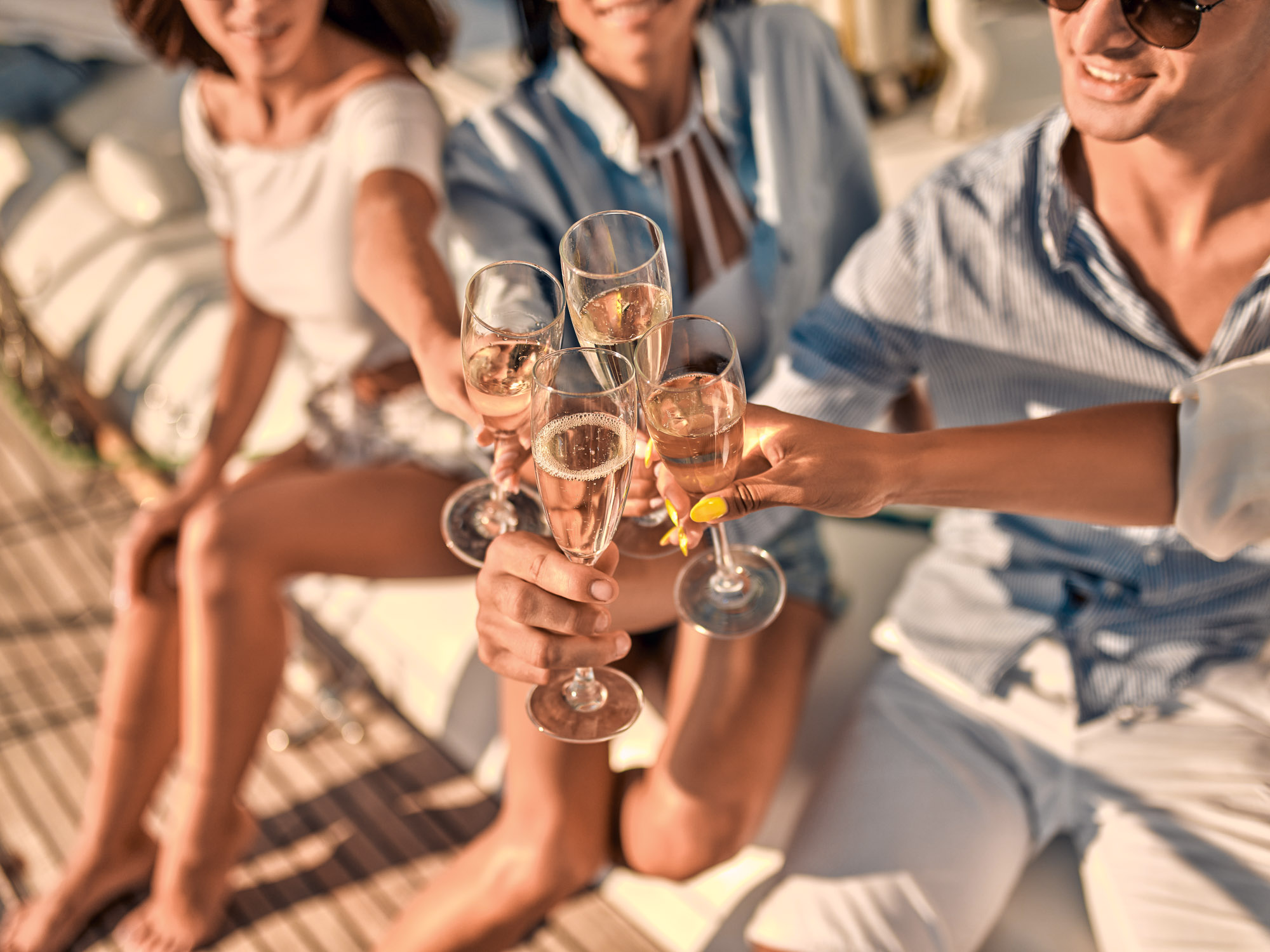 Cheers! Cropped image of group of friends relaxing on luxury yacht and drinking champagne. Having fun together while sailing in the sea. Traveling and yachting concept.